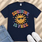 A navy blue t-shirt with a colorful sun graphic and the text "SUNSHINE IS FREE" printed on it, along with a pair of jeans and white sneakers.