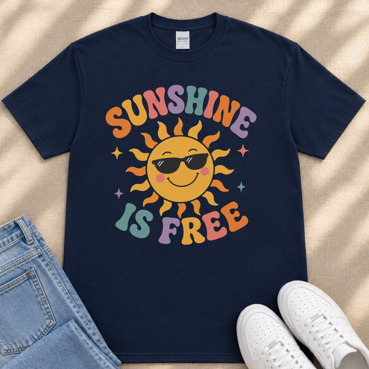 A navy blue t-shirt with a colorful sun graphic and the text "SUNSHINE IS FREE" printed on it, along with a pair of jeans and white sneakers.