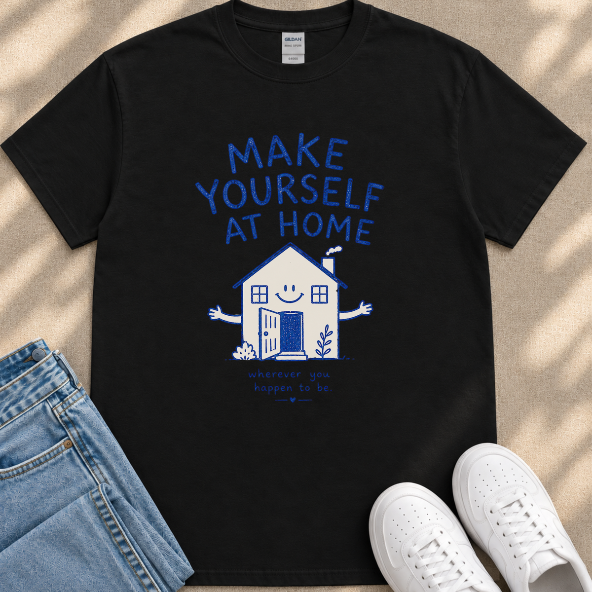 A black t-shirt with a graphic design of a house and the text "MAKE YOURSELF AT HOME" printed on it, along with a smaller text below that says "Wherever you go, good things happen to you."