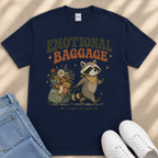 a navy blue t-shirt with a graphic design depicting a raccoon pulling a suitcase filled with various items, accompanied by the text "Emotional Baggage" and "(CAREY-ON SIZE)".