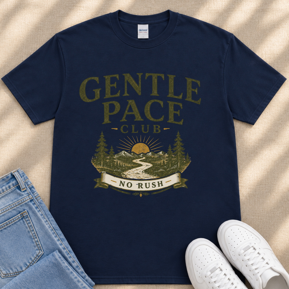 A navy blue t-shirt with a graphic design featuring a mountain landscape, a banner with the text "GENTLE PACE CLUB" and "NO RUSH", and a pair of jeans and white sneakers.