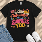 A black t-shirt with a colorful graphic design featuring text and various decorative elements such as flowers, stars, and a sun.