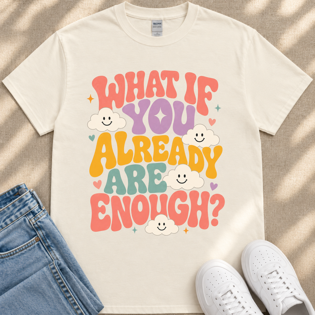 A white t-shirt with a colorful graphic design featuring the text "What If You Already Are Enough?" surrounded by smiling clouds.