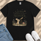 A black t-shirt with a whimsical graphic design depicting a rabbit gazing up at a telescope, surrounded by a forest scene with mushrooms and flowers.