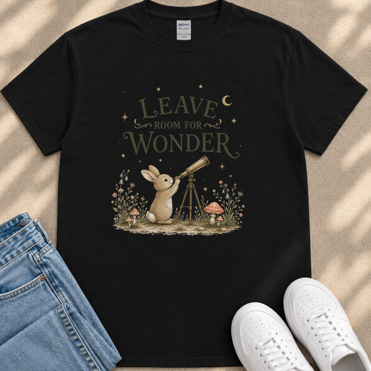 A black t-shirt with a whimsical graphic design depicting a rabbit gazing up at a telescope, surrounded by a forest scene with mushrooms and flowers.