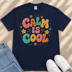 A navy blue t-shirt with a colorful graphic design that says "Calm is cool" surrounded by various decorative elements such as flowers, stars, and smiley faces.