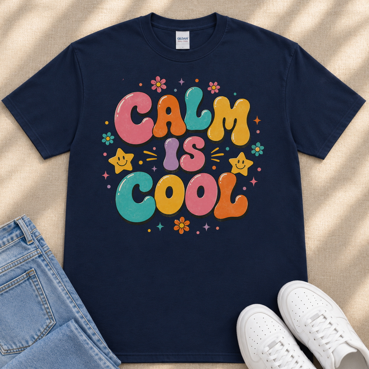 A navy blue t-shirt with a colorful graphic design that says "Calm is cool" surrounded by various decorative elements such as flowers, stars, and smiley faces.