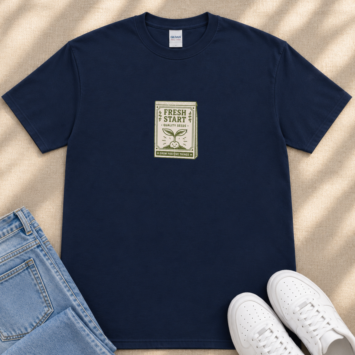 A navy blue t-shirt with a green and white label that says "FRESH START" and a graphic of a plant, along with a pair of blue jeans and white sneakers.