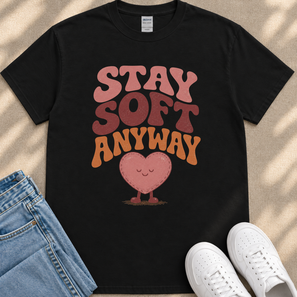A black t-shirt with a graphic design featuring a heart and the text "STAY SOFT ANYWAY" in a playful, retro style.