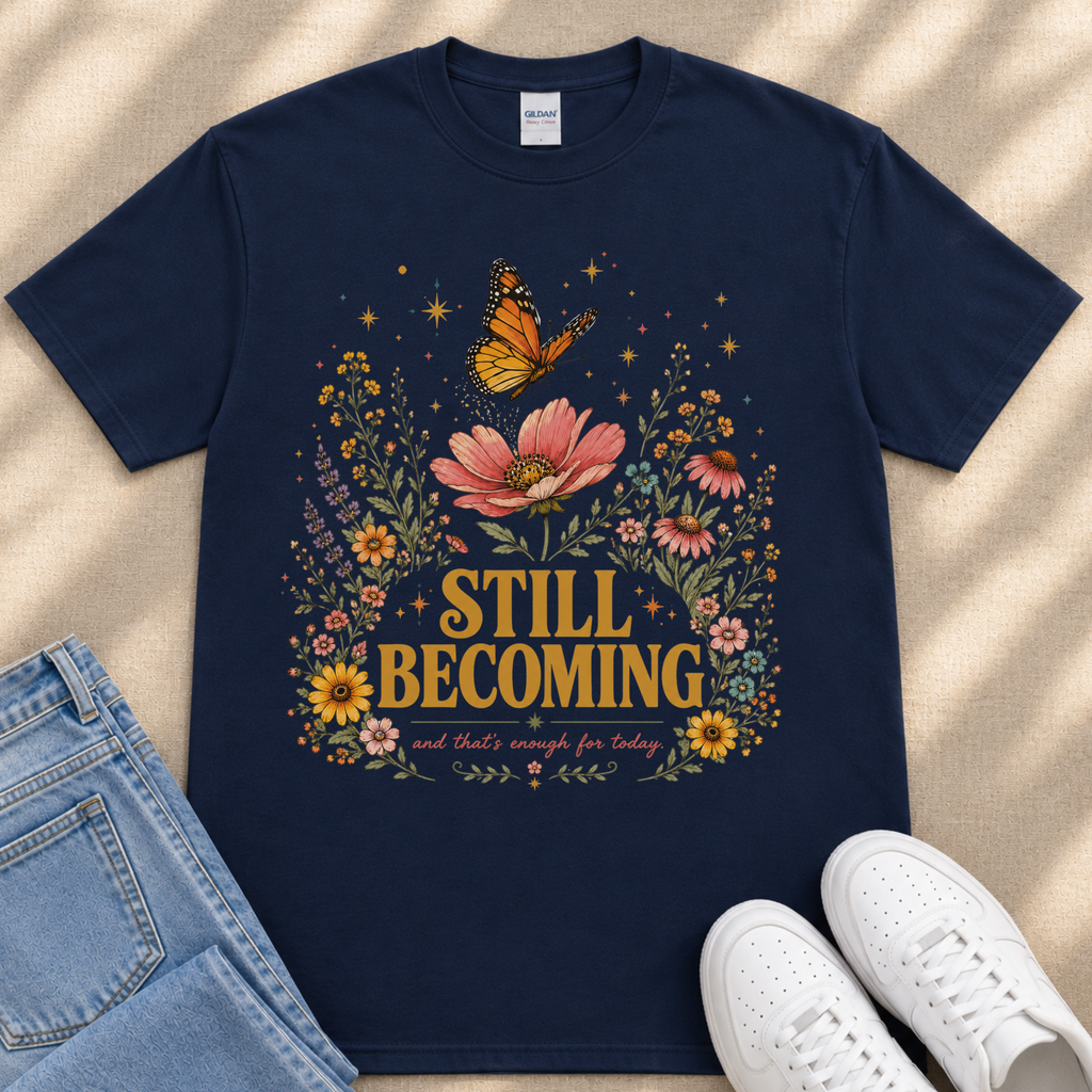 A navy blue t-shirt with a floral design and the text "STILL BECOMING" printed on it, along with a pair of jeans and white sneakers.