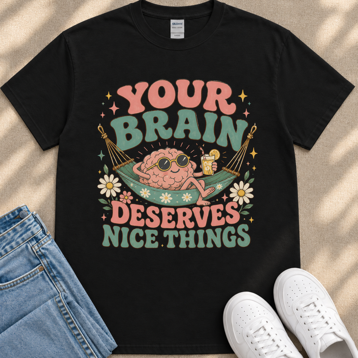 A black t-shirt with a colorful graphic design featuring a cartoon brain character in a hammock, surrounded by flowers and text that reads "Your brain deserves nice things".