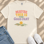 A white t-shirt with a colorful graphic design and text, along with a pair of jeans and white sneakers, all laid out on a surface.
