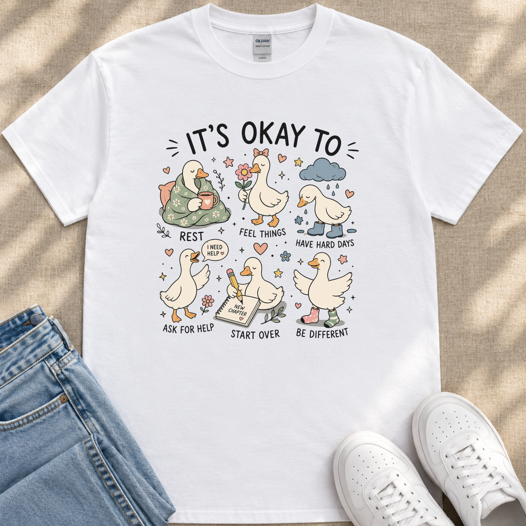 A white t-shirt with a graphic design depicting a series of cartoon ducks and text that encourages positive thinking and self-care.
