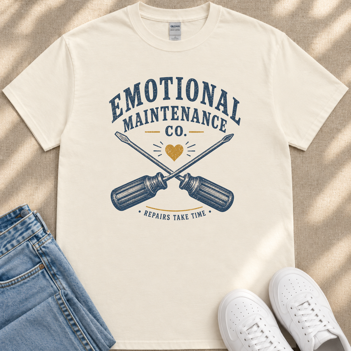 A white t-shirt with a graphic design featuring a crossed wrench and the text "Emotional Maintenance Co."