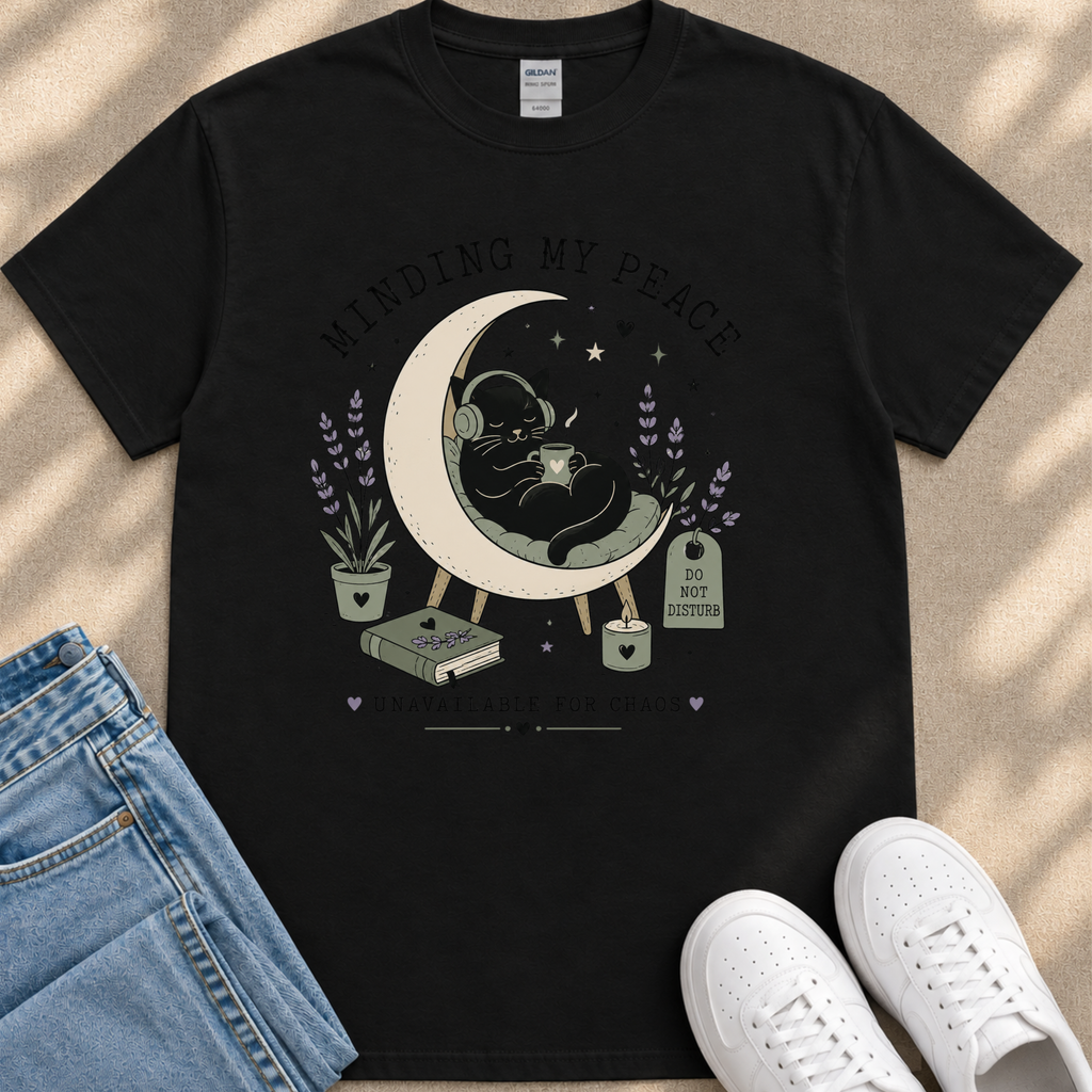 A black t-shirt with a graphic design depicting a cat sitting on a crescent moon, surrounded by flowers and plants, with the text "MINDING MY PEACE" and "UNAVAILABLE FOR CHOSEN" printed on it.