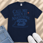 A navy blue t-shirt with a graphic design of a telephone and the text "Call me when it makes sense" printed on it, along with a small orange star. The t-shirt is placed next to a pair of blue jeans and white sneakers.