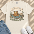 a white t-shirt with a cartoon image of a beaver in a hot tub, surrounded by various objects such as a cup, a plant, and a pair of sunglasses. The text on the t-shirt reads "DEEPLY UNAIVABLE".