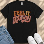 A black t-shirt with the text "FEEL IT ANYWAY" printed on it, along with a pair of blue jeans and white sneakers.