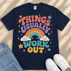 A navy blue t-shirt with a colorful graphic design that says "THINGS USUALLY WORK OUT" and features a rainbow, clouds, stars, and a smiley face.