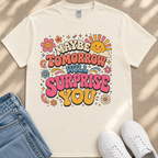 A white t-shirt with a colorful graphic design featuring text and various decorative elements such as flowers, stars, and a sun.