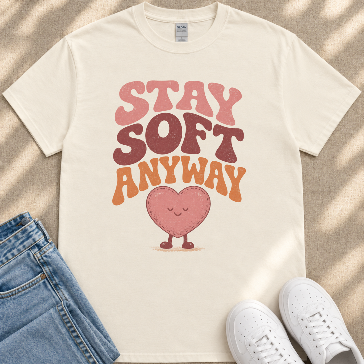 A white t-shirt with a heart-shaped graphic and the text "STAY SOFT ANYWAY" printed on it, along with a pair of jeans and white sneakers.