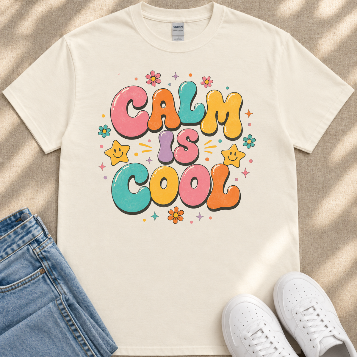 A white t-shirt with a colorful graphic design that says "Calm is cool" surrounded by various decorative elements such as flowers and stars.