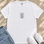 A white t-shirt with a graphic design, a pair of blue jeans, and white sneakers are arranged on a beige surface.