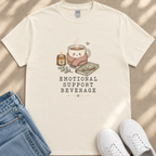A white t-shirt with a graphic design depicting a cup of coffee, a candle, and a book, along with the text "EMOTIONAL SUPPORT BEVERAGE".