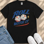 A black t-shirt with a graphic design featuring two dice with a smiley face, along with the text "Roll with it" and a red and blue stripe. The t-shirt is placed next to a pair of jeans and white sneakers.