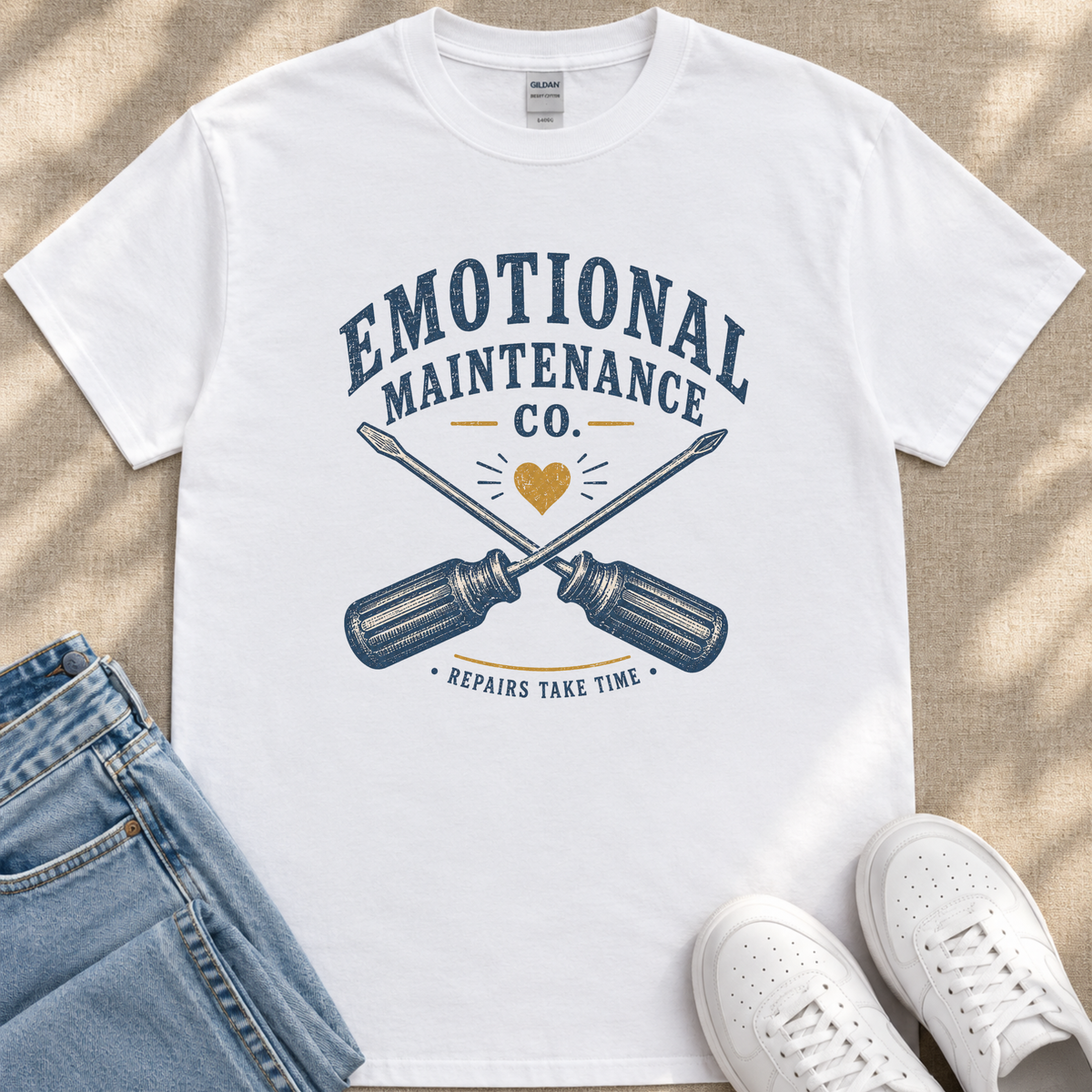 A white t-shirt with a graphic design featuring a crossed wrench and the text "Emotional Maintenance Co."