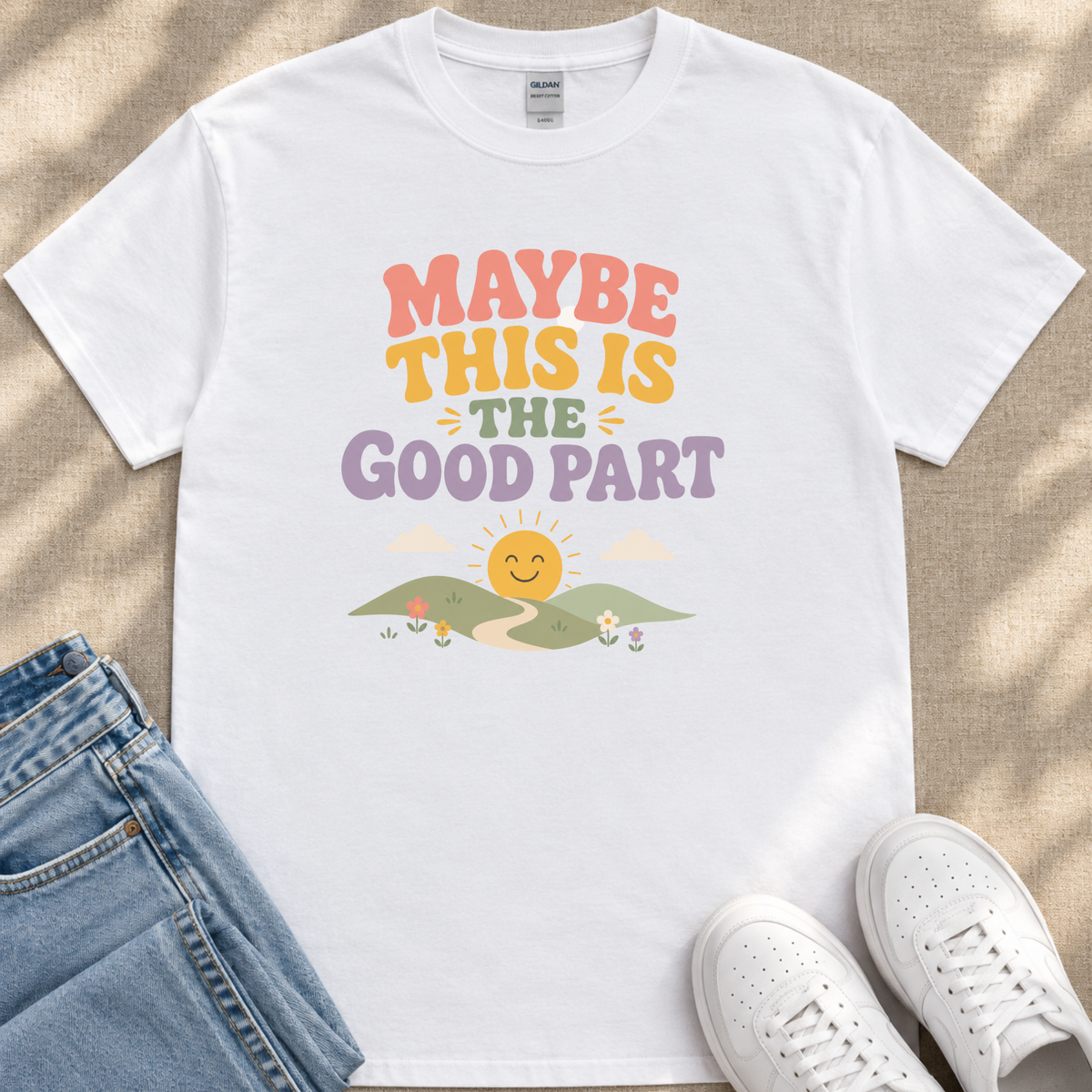 A white t-shirt with a colorful graphic design and text, along with a pair of jeans and white sneakers, all laid out on a surface.