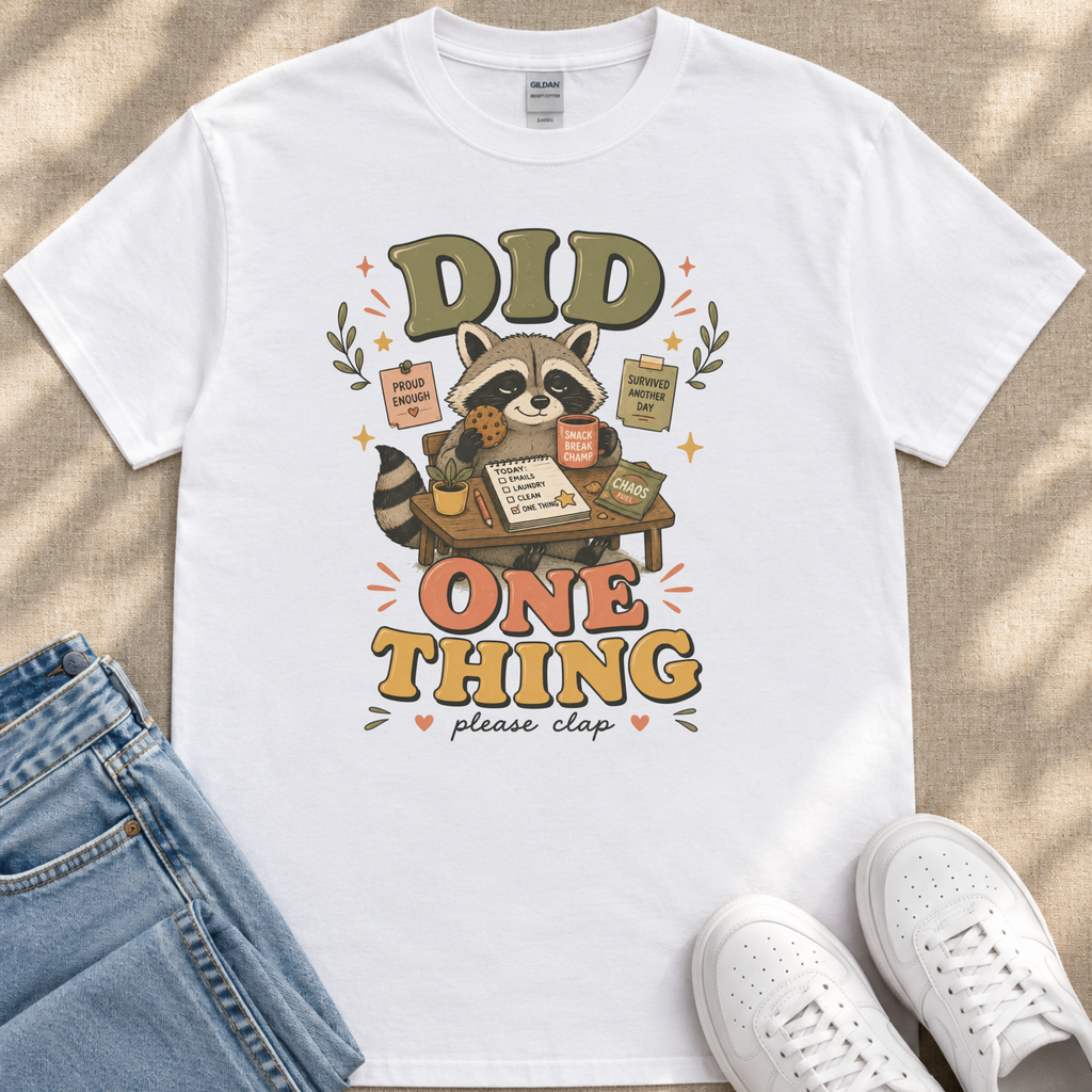 A white t-shirt with a graphic design featuring a raccoon holding a sign that says "Did One Thing" and surrounded by various objects.