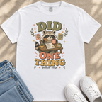 A white t-shirt with a graphic design featuring a raccoon holding a sign that says "Did One Thing" and surrounded by various objects.