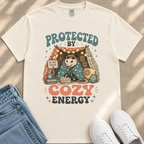 A white t-shirt with a graphic design featuring an opossum wearing a cozy blanket and surrounded by various objects, including a tent, snacks, and a sign that says "Do not enter".