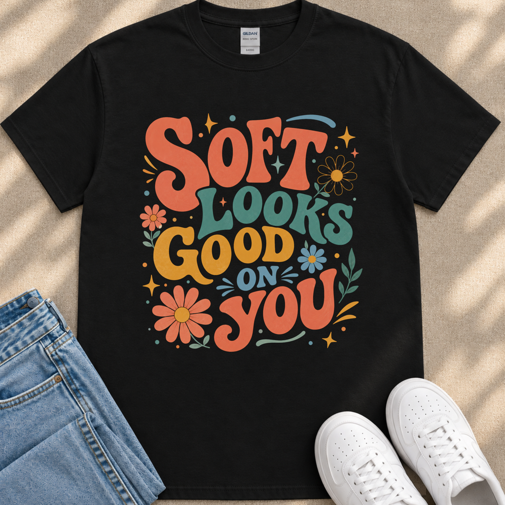 A black t-shirt with a colorful graphic design that says "Soft looks good on you" surrounded by flowers and stars.