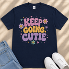 A navy blue t-shirt with a colorful graphic design and text, along with a pair of jeans and white sneakers, all laid out on a surface.