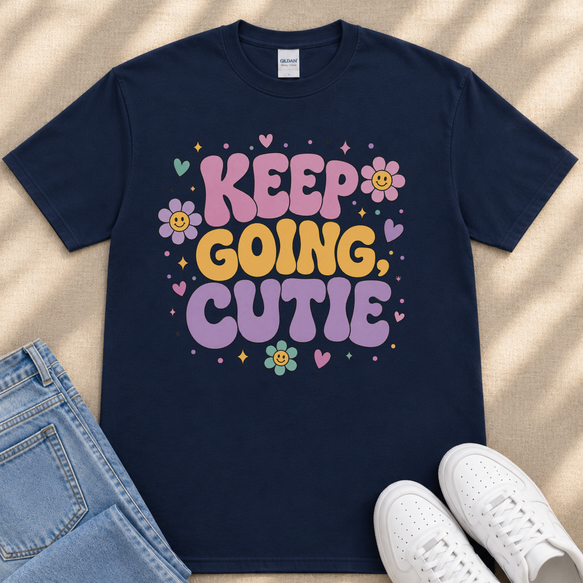 A navy blue t-shirt with a colorful graphic design and text, along with a pair of jeans and white sneakers, all laid out on a surface.
