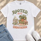 A white t-shirt with a graphic design featuring a potted plant, a stack of books, and a pair of headphones, along with the text "ROOTED BUT UNBOTHERED".