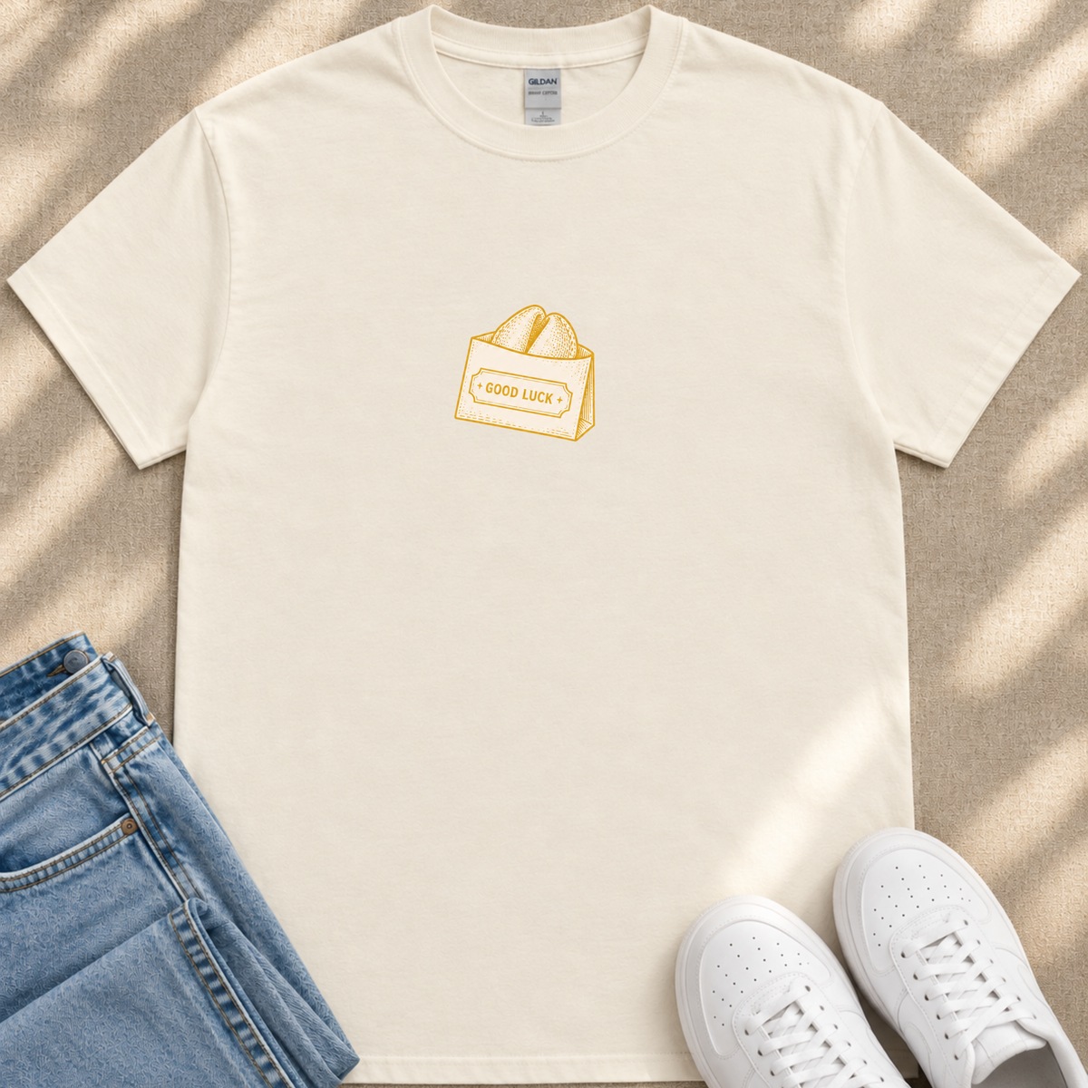 A white t-shirt with a graphic of a bag of bread and the text "GOOD LUCK" printed on it, along with a pair of blue jeans and white sneakers.